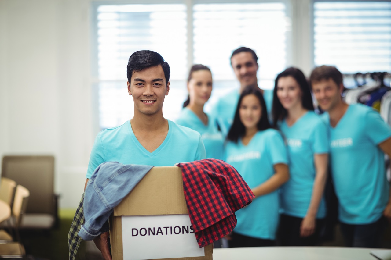 A young man holding a box of donations with his volunteer friends in the background